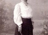 historische Aufnahme von Frau mit Hut, Bluse, langem Rock und einer Art Tennisschläger