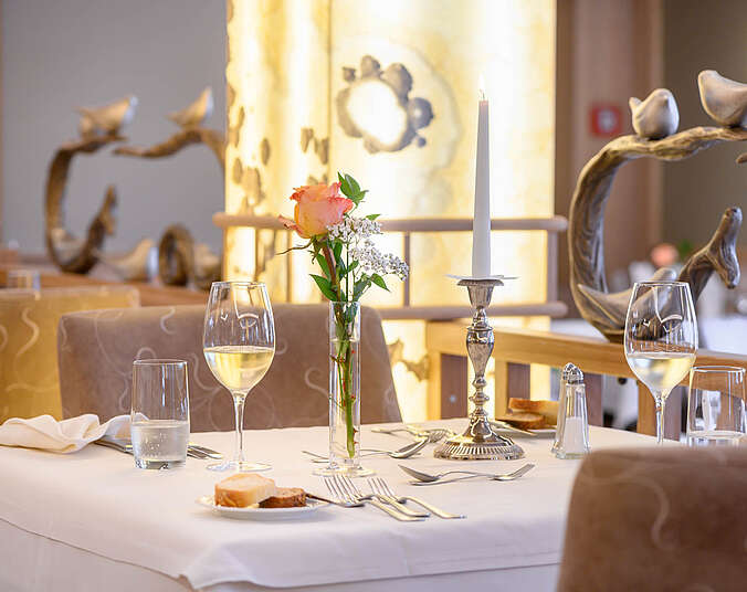 Ansprechend eingedeckter Tisch mit Kerzenleuchter und Blumen, Besteck und Weisswein.