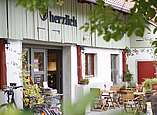 Schönes Bauernhaus mit Schriftzug herzlich. Vor dem Haus huebsch dekorierte Holztische mit Blümchen.