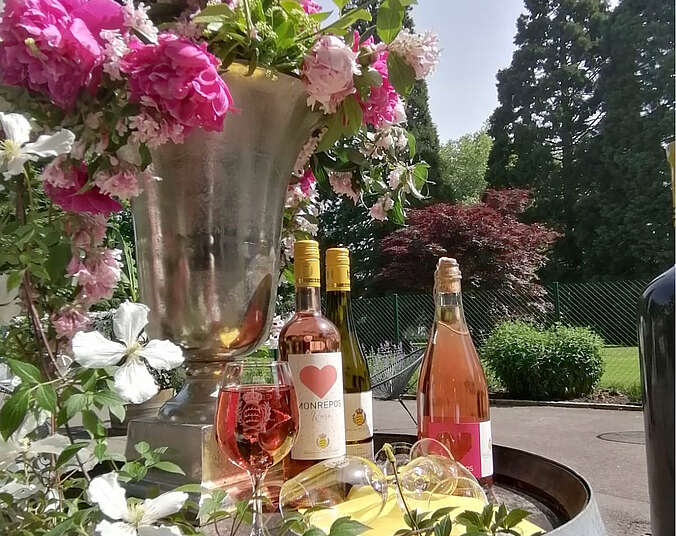 Blumen, Weinflaschen und gefüllte Weingläser hübsch dekoriert auf einem Weinfass.
