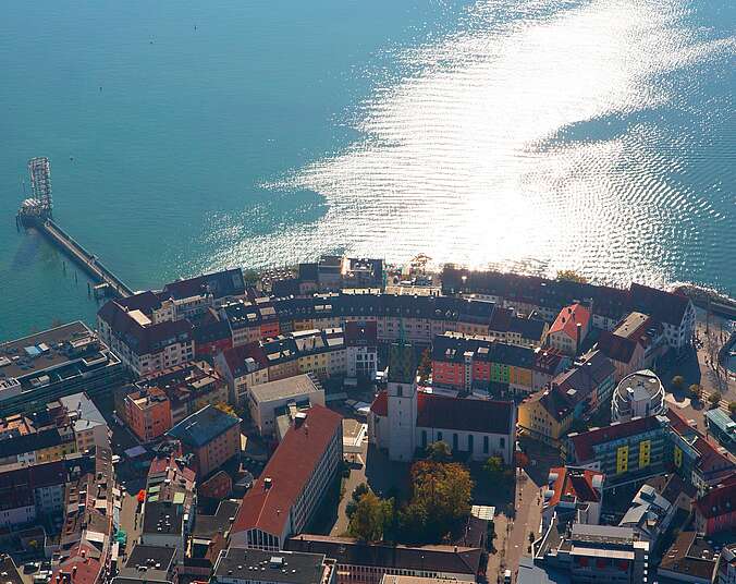 Blick von oben auf Friedrichshafen mit der Nikolauskirche, den Moleturm und den Bodensee.