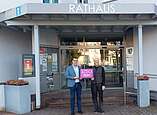 Ailingens Ortsvorsteher Andreas Lipp (links) präsentiert mit Agenturchef Dirk Holstein, HOME.digital, das Jubiläumslogo. (Foto: Ortsverwaltung Ailingen)