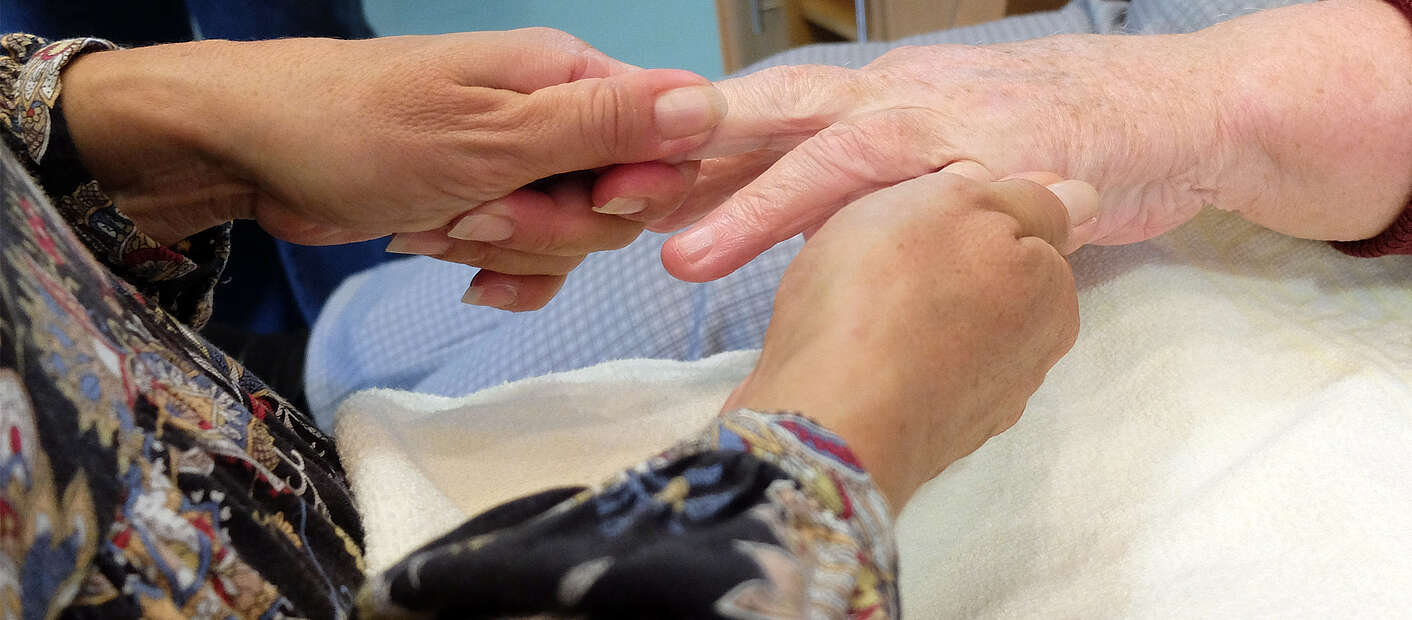 Pflegerin cremt Seniorin Hände ein
