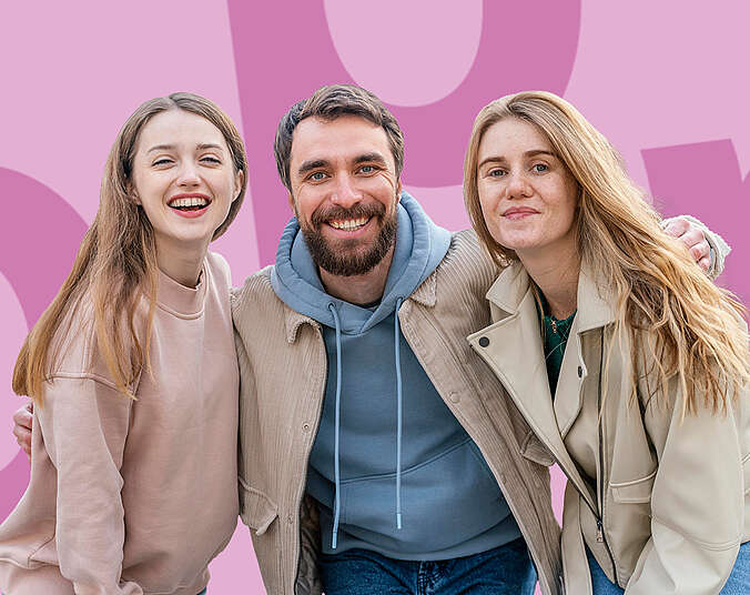 Zwei jugendliche Frauen in beigen Oberteilen rahmen links und rechts einen Mann mittleren Alters mit Bart un blauem Hoodie ein. Sie wirken hehiter und gelöst vor einem rosa-pinken Hintergrund..