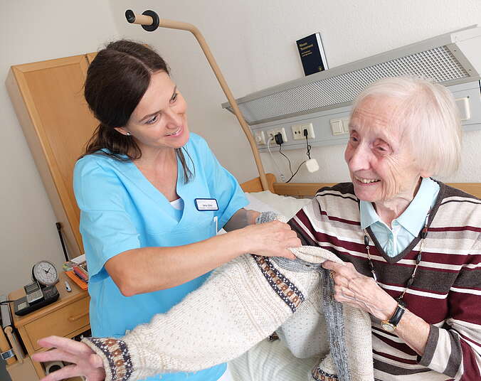 Pflegerhin hilft seniorein beim Jacke anziehen