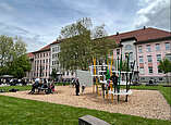 Schulhof mit neuer Rasenfläche und Spielgeräten, Kinder spielen an Spielgeräten
