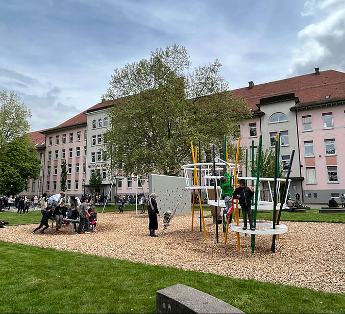 Schulhof mit neuer Rasenfläche und Spielgeräten, Kinder spielen an Spielgeräten