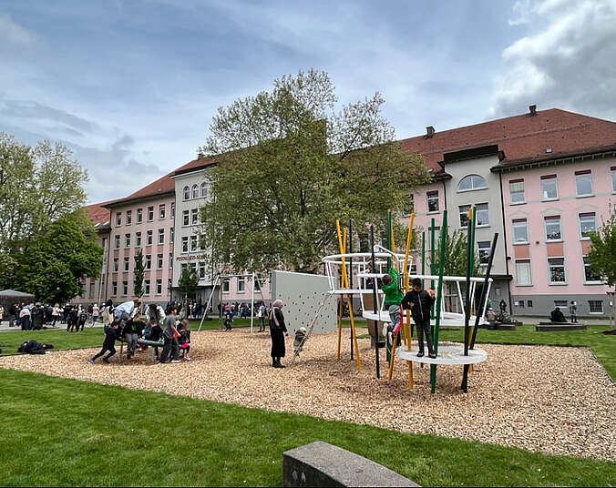 Schulhof mit neuer Rasenfläche und Spielgeräten, Kinder spielen an Spielgeräten