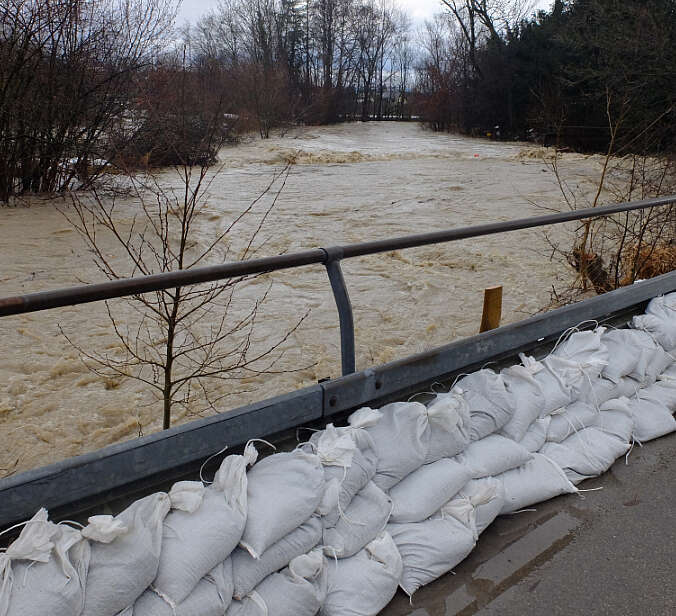 Sandsäcke entlang von Leitplanke sollen Hochwasser von Fluss zurückhalten