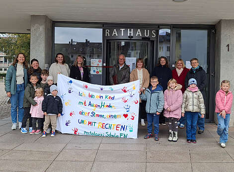 Kinder und Erwachsene vor dem Rathaus mit einem großen weißen Transparent