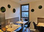 Café Ecke mit modernen Holztischen und Stühlen, Moosbilder an der Wand.